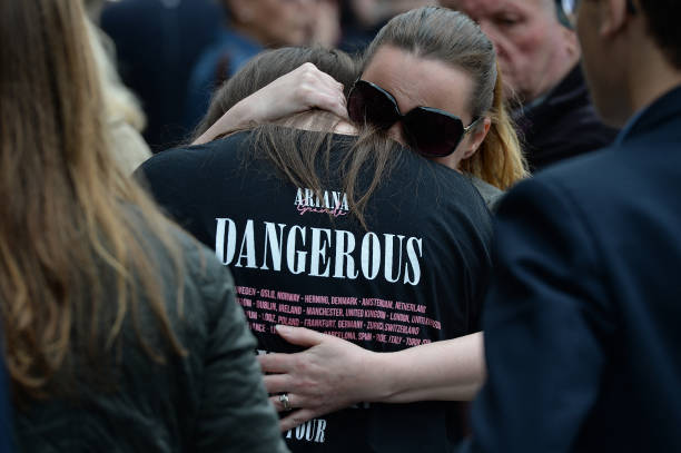 Woman hugs a girl, wearing a t-shirt from Ariana Grande's Dangerous Woman near floral tributes in Albert Square in Manchester, northwest England on May 24 following the May 22 terror attack at the Manchester Arena. Police on Tuesday named Salman Abedi -- reportedly British-born of Libyan descent -- as the suspect behind a suicide bombing that ripped into young fans at an Ariana Grande concert at the Manchester Arena on May 22, as the Islamic State group claimed responsibility for the carnage. — frame 2/3 (612×407)