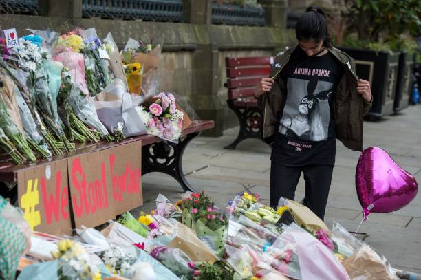 Girl, wearing a t-shirt from Ariana Grande's Dangerous Woman Tour, poses for a photograph alongside flowers in Albert Square in Manchester, northwest England on May 24 placed as tributes to the victims of the May 22 terror attack at the Manchester Arena. Police on Tuesday named Salman Abedi -- reportedly British-born of Libyan descent -- as the suspect behind a suicide bombing that ripped into young fans at an Ariana Grande concert at the Manchester Arena on May 22, as the Islamic State group claimed responsibility for the carnage. / AFP PHOTO / CHRIS J RATCLIFFE — frame 3/3 (612×407)