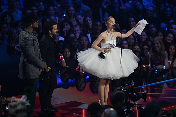 Singer-songwriter Ariana Grande accepts the award for Video of the Year for "Brighter Days Ahead", flanked by host US rapper LL Cool J and US music video director Christian Breslauer on stage during the MTV Video Music Awards at UBS Arena in Elmont, New York, on September 7, 2025. — frame 107/109 (612×408)